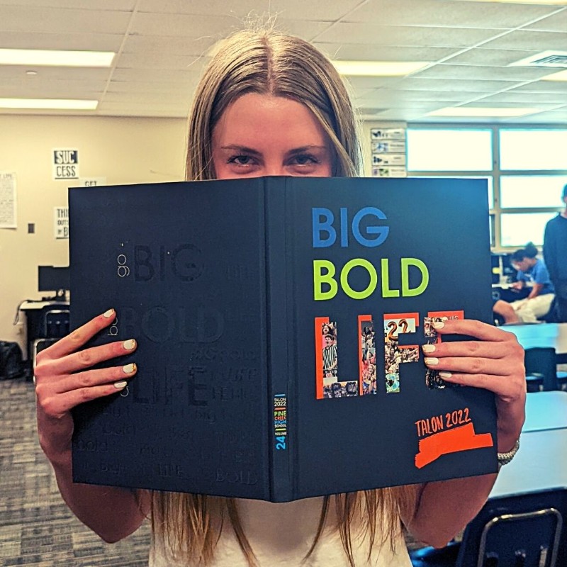 Student with yearbook in front of face.